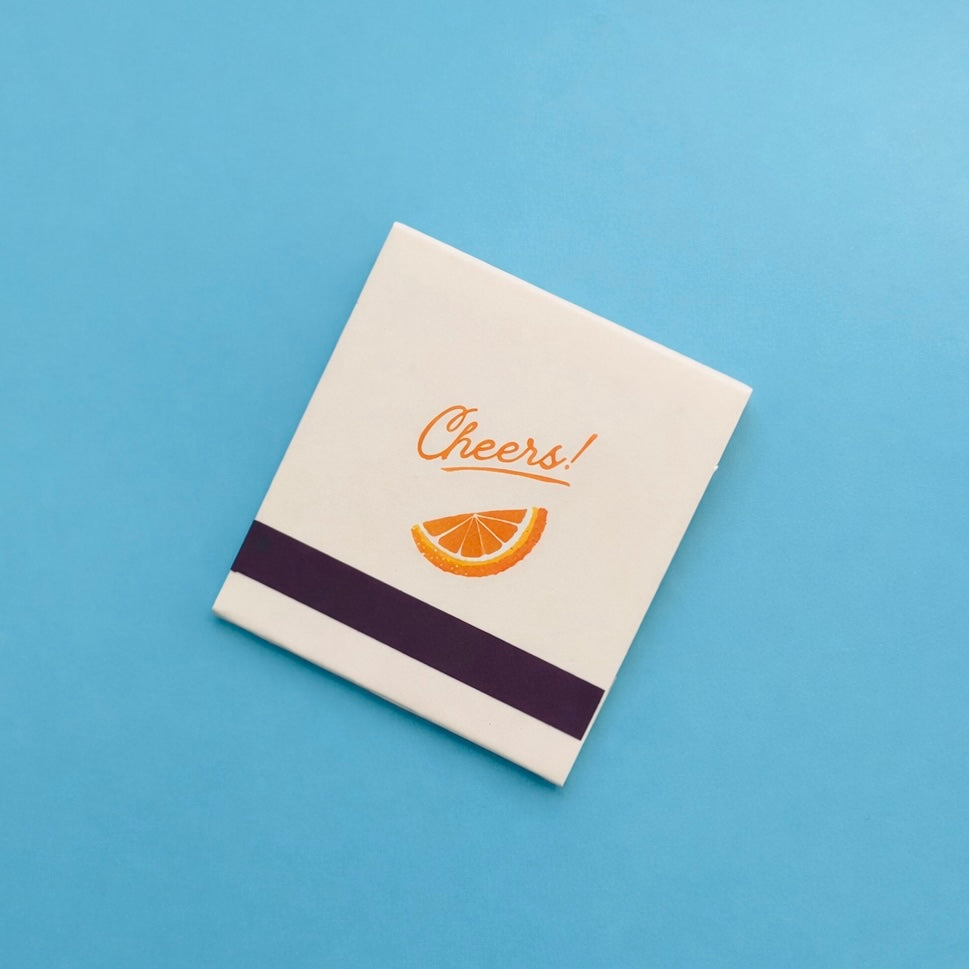 Back of Negroni matchbook featuring an orange slice and the word “Cheers” with the match-striking bar at the bottom