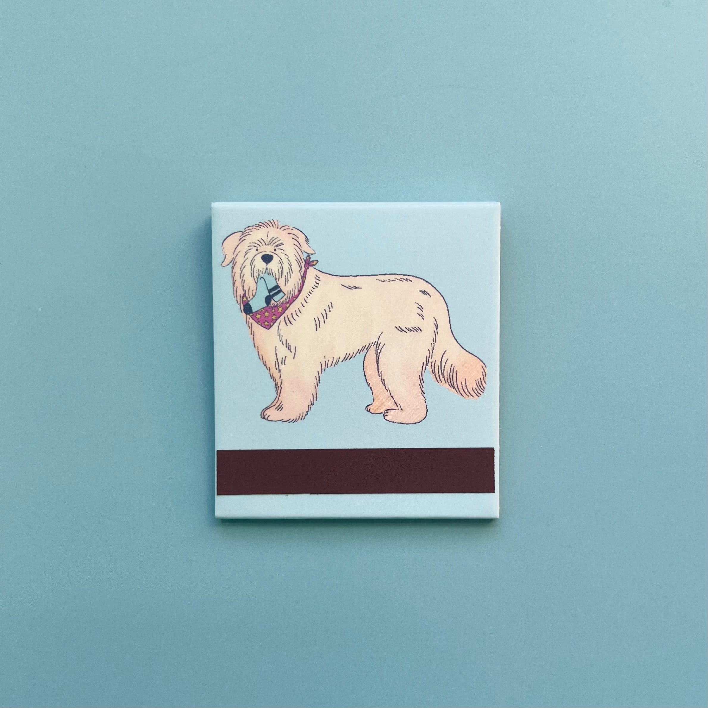 Back of dog matchbook depicting a Soft-Coated Wheaten Terrier with socks in its mouth and the match-striking bar at the bottom