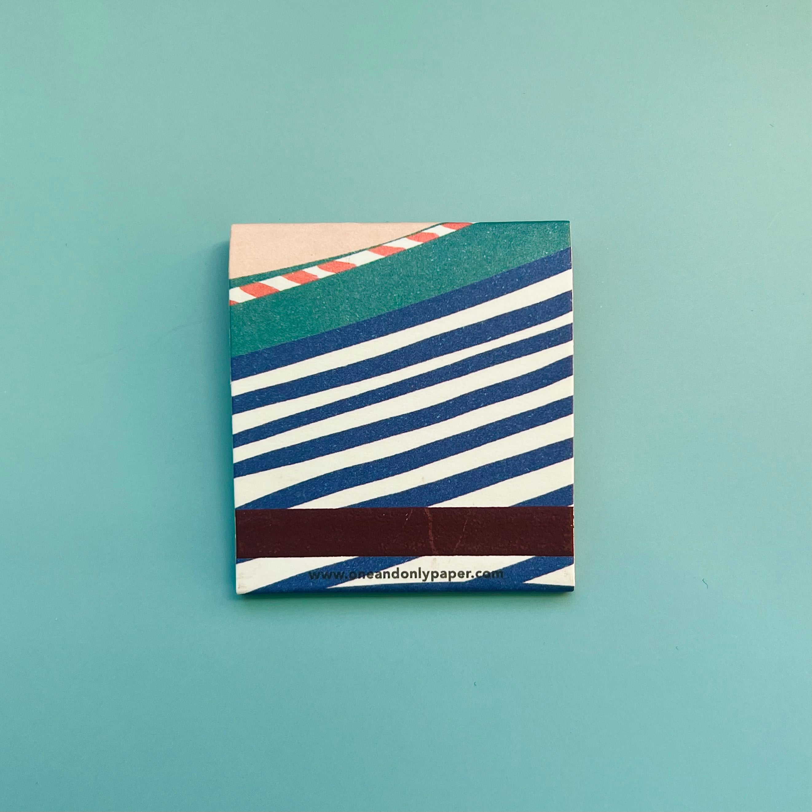 Back of race car matchbook featuring a drawing of a race track with the match-striking bar on the bottom